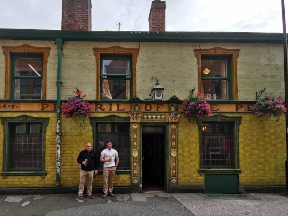 The Peveril of the Peak pub in Manchester — green and yellow tiled facade with hanging flower baskets