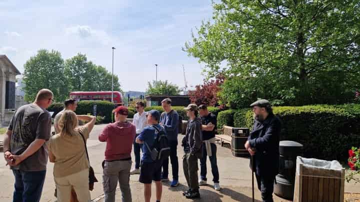 Tour group in a London park with a red double-decker bus behind